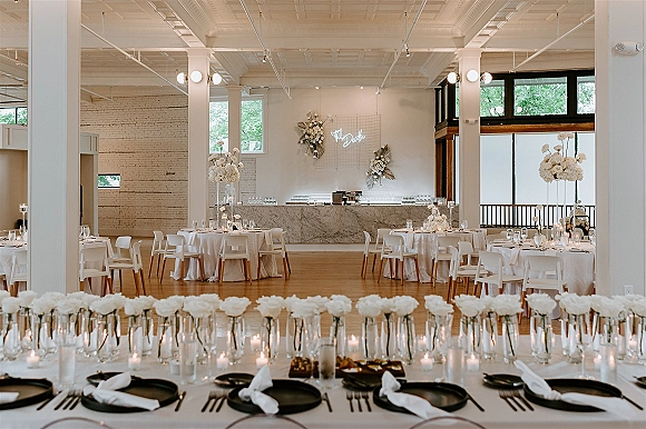 Reception tablescape with round table wedding setup featuring white linens, black plates, candlelit floral centerpieces in a bright loft venue