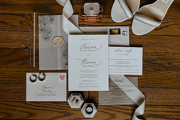 Invitation suite wedding invitation flat lay with calligraphy cards, RSVP, envelopes, wax seal, ribbon, rings, perfume on wood tabletop