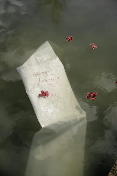 Vow letter with handwritten vows on translucent vellum paper, gently floating on a calm pond, water ripples softly framing the keepsake.