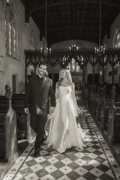 Ceremony recessional as the couple walks down the aisle, holding hands past glowing candles, beneath stained glass in a vaulted church.