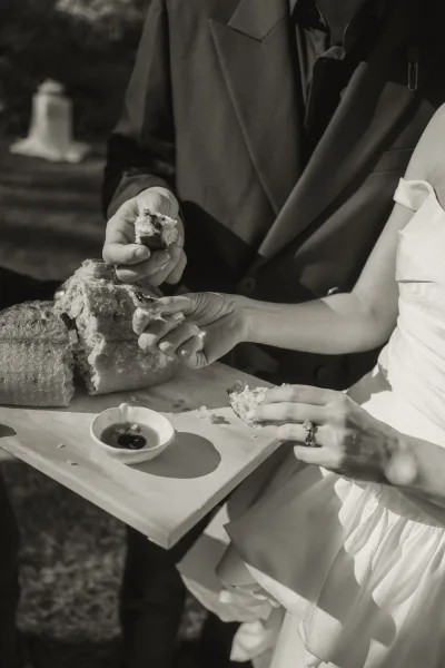 Bread breaking moment with a couple sharing bread, dipping pieces into an olive oil dish in a sunlit garden, shadows across the lawn.