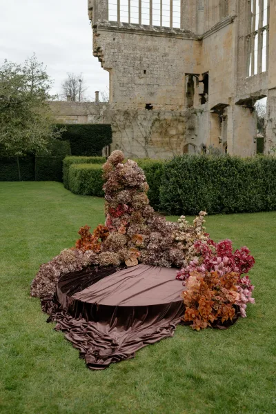 Ceremony backdrop featuring a wedding floral installation with dried florals, set before weathered stone ruins.