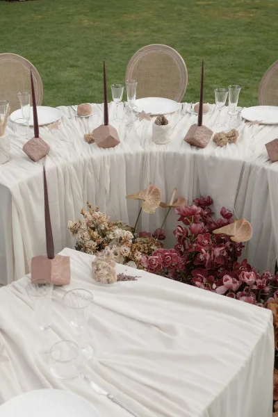 Reception tablescape on an outdoor reception table, anchored by taper candles, set across a grass lawn.