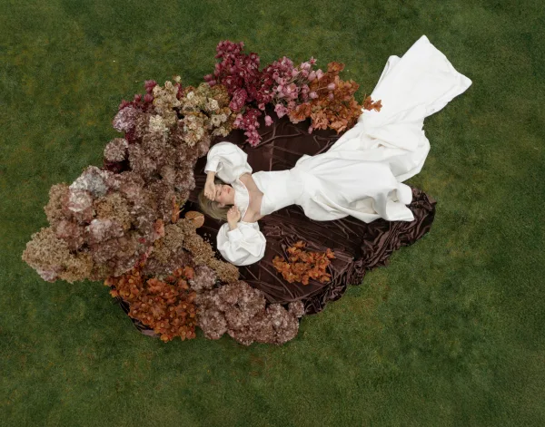Bridal portrait in an overhead bridal photo of a bride lying on a grass lawn, wearing a puff sleeve gown accented with dried florals.