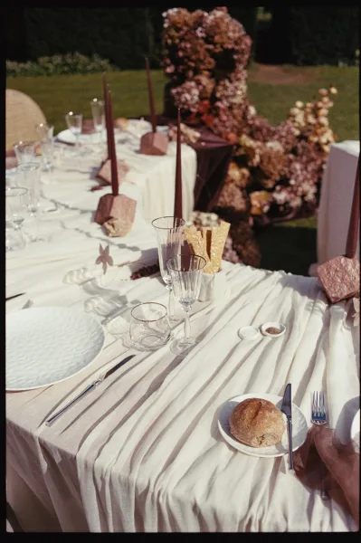Reception tablescape on an outdoor reception table with brown taper candles, set on a grass lawn bordered by hedges for an al fresco feel.