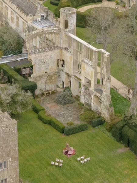Outdoor ceremony setup with garden ceremony seating facing a floral altar, set before stone ruins on a grass lawn with pathways.