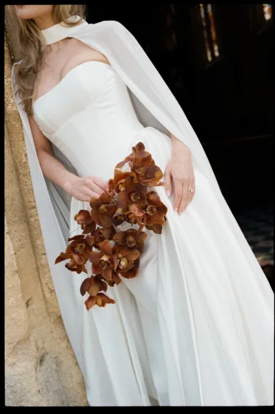 Wedding dress close-up captures a strapless wedding gown with corset bodice and an orchid bouquet, set against dim stone walls and stained glass.