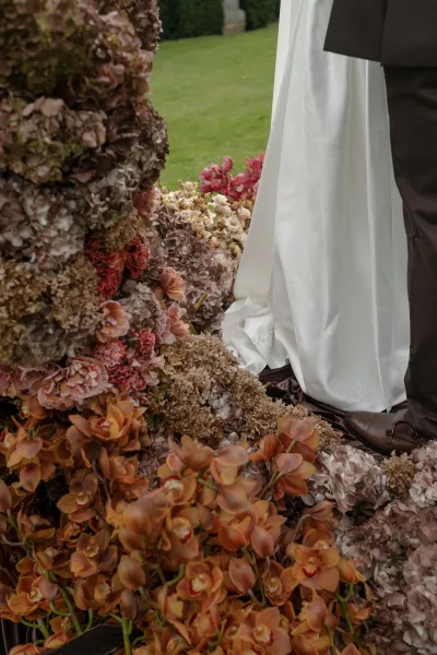 Ground floral installation serving as the ceremony aisle flowers with orchids, set on a grass lawn edged by garden hedges.