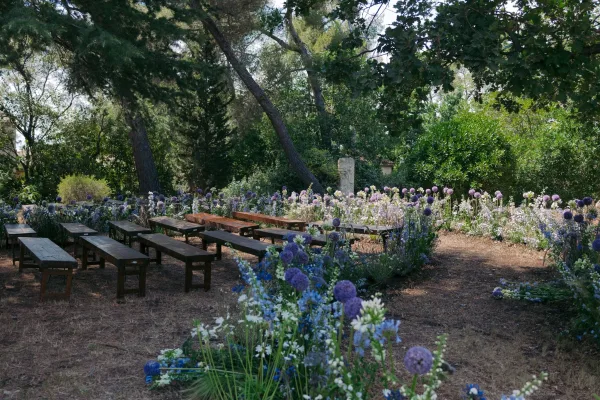 Outdoor ceremony setup with woodland ceremony seating on wooden benches beneath trees along a natural dirt path amid lush garden greenery