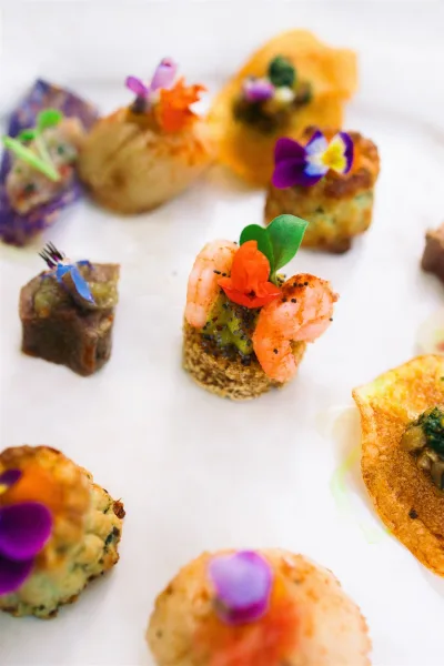 Wedding appetizers arranged as cocktail hour canapés, topped with edible flowers for a colorful, elegant bite-sized presentation.