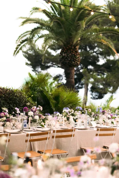 Reception tablescape for an outdoor reception table with white taper candles, set under palm trees amid garden greenery and sky.