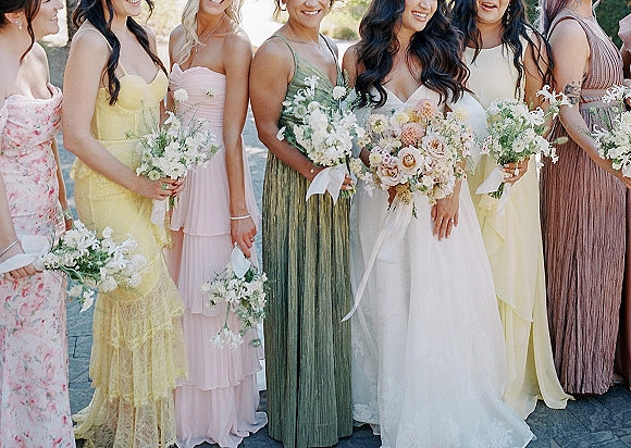 Bridesmaid group photo with bride with bridesmaids holding bridal party bouquets in pastel dresses on stone pavement in outdoor light