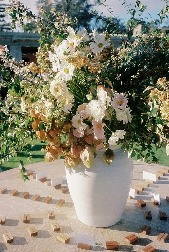 Wedding centerpiece with wildflower wedding centerpiece in a white ceramic vase, daisies and cosmos, with escort cards on an outdoor lawn
