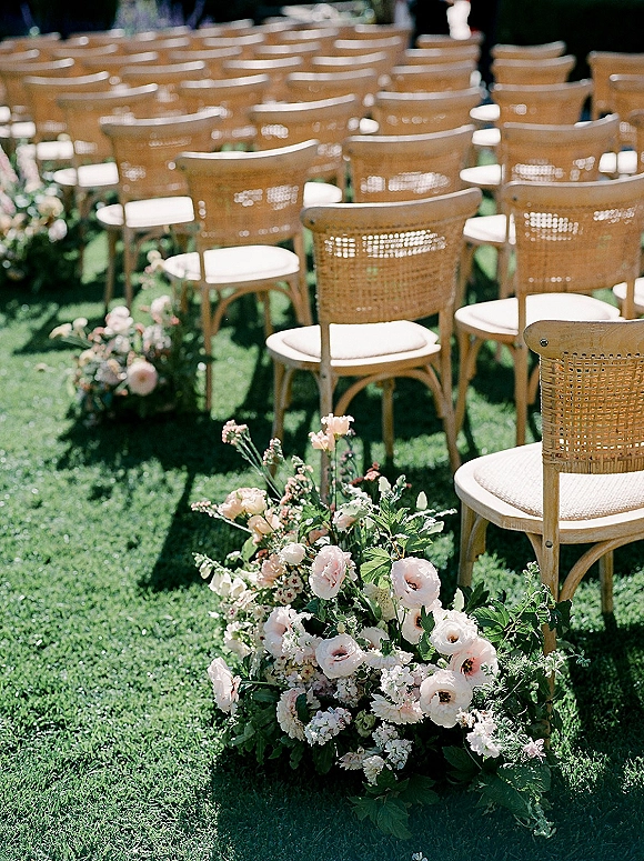 Ceremony aisle decor with outdoor wedding ceremony seating, woven wood chairs and low floral ground arrangements on a garden lawn