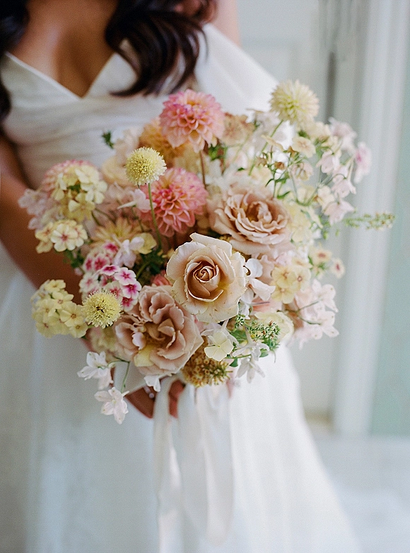 Bridal bouquet of garden rose bouquet blooms with dahlias in blush and cream, tied with a white ribbon against a soft neutral backdrop