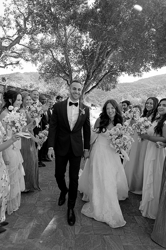 Wedding recessional as bride and groom walking past lined-up bridal party on a stone patio, bouquet and long veil with mountain backdrop