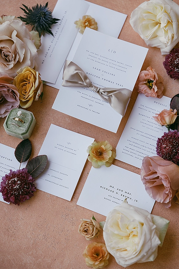 Invitation suite wedding invitation flat lay with silk ribbon bow, rings and ring box, roses and ranunculus on linen backdrop