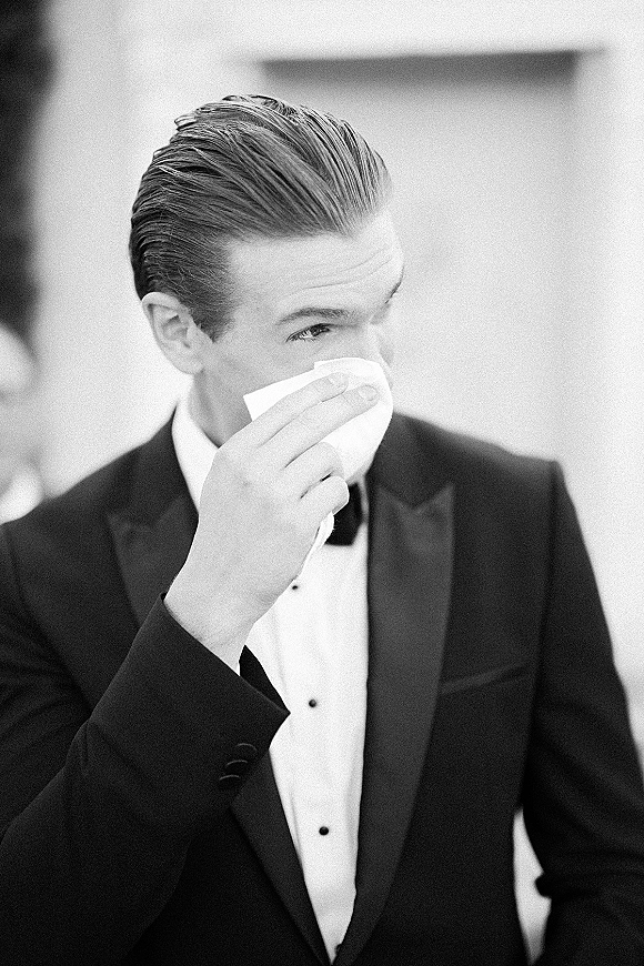 Groom portrait of an emotional groom photo wiping tears with a handkerchief, wearing a black tuxedo and bow tie indoors