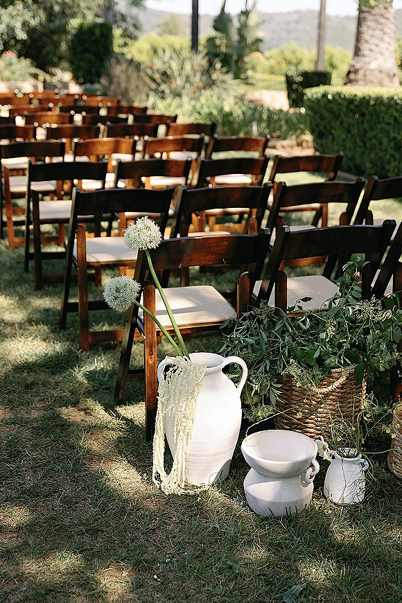 Ceremony seating with outdoor ceremony chairs in neat rows, wood folding chairs and cushions flanking a greenery garland aisle on a sunny lawn
