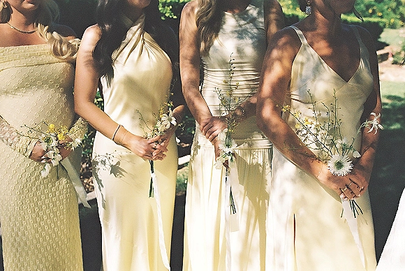 Bridesmaid dresses in champagne bridesmaid dresses with wrist corsages and small bouquets, standing on a sunlit garden lawn with shadows