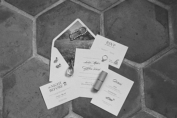 Invitation suite wedding invitation flat lay with RSVP and details cards, wax seal, wedding ring, and pearl bracelet on hexagon tile floor