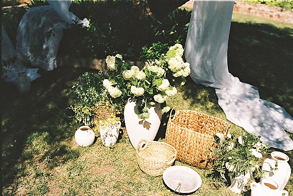 Wedding floral decor with hydrangea wedding flowers in ceramic vases and woven baskets, arranged low on a sunlit grass lawn with greenery