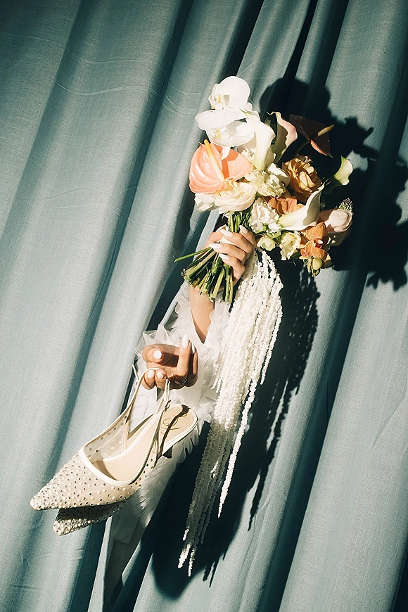 Bridal bouquet cascading with white orchids and calla lilies, peach anthurium, and ribbon streamers against a teal drape backdrop