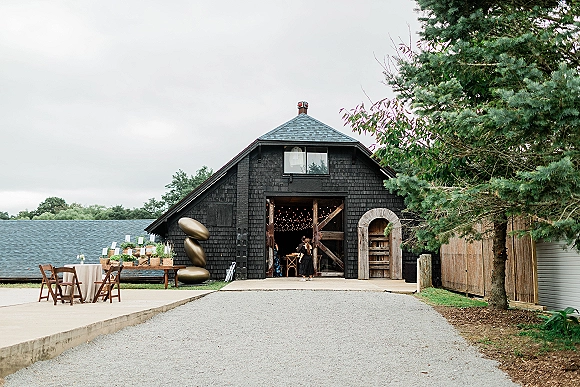 Barn wedding reception with a barn reception entrance, wood folding chairs and linen tables under string lights beside open black barn doors.
