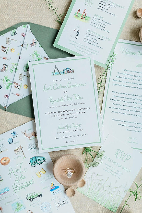 Invitation suite with watercolor wedding invitations, RSVP and map cards, greenery sprigs, and rings on a linen fabric backdrop