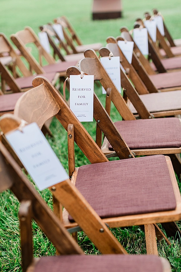 Ceremony seating with outdoor ceremony chairs, wood folding chairs on a grass lawn, featuring reserved seat tags tied with string