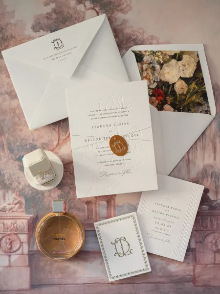Invitation suite with letterpress wedding invitations, envelopes, wax seal, monogram crest, ring box and perfume on a painted scenic backdrop