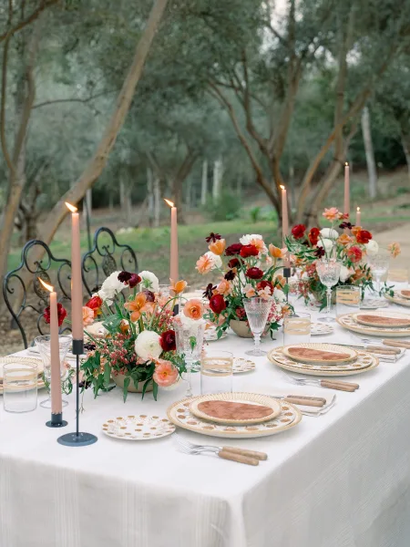 Reception tablescape with an outdoor wedding tablescape feel, featuring floral centerpieces and taper candles on a white tablecloth in a garden setting