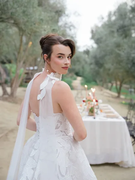 Bridal portrait of bride looking over shoulder in a lace wedding dress and long veil, pearl earrings, on a soft daylight garden path