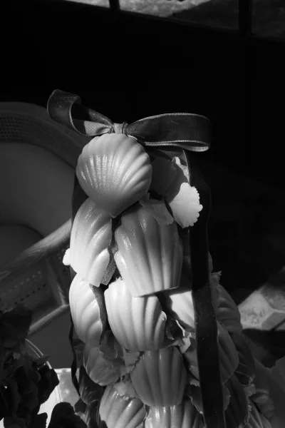 Madeleine tower as a wedding dessert display, tied with a soft ribbon, with a wicker chair, window panes, and tile floor in the background.