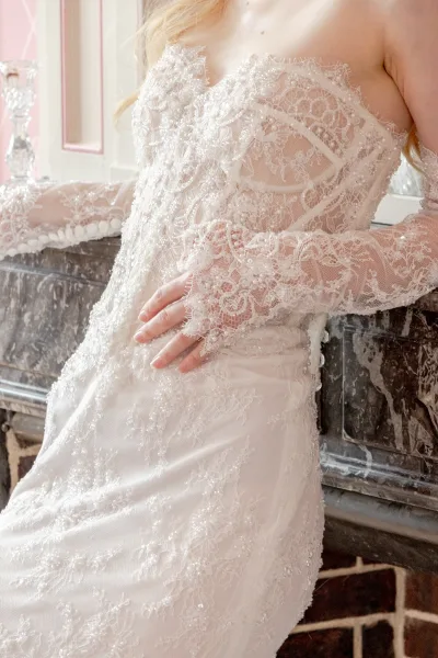 Wedding dress close-up of a lace bridal gown with delicate pearls along the bodice, framed by a marble mantel and a crystal candlestick.