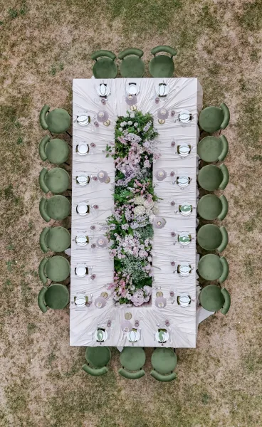 Reception tablescape for an outdoor reception table featuring a lush floral runner, arranged on a grass lawn with an elegant, airy ambience.