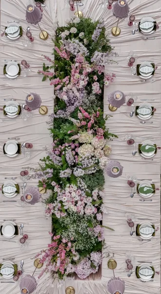 Reception tablescape featuring a floral table runner of pastel blooms on ruched table linen, accented by brass table lamps.