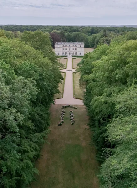 Estate wedding venue centered on a fountain, with an aisle on the lawn framed by trees and a curving pathway beneath an open sky.