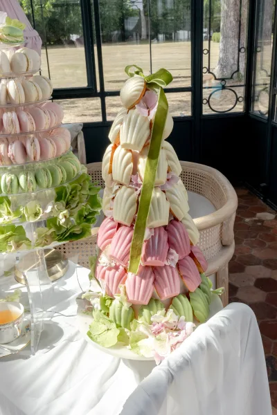 Dessert tower of madeleines forming a madeleine tower, finished with a ribbon, by glass windows overlooking a garden lawn and trees.