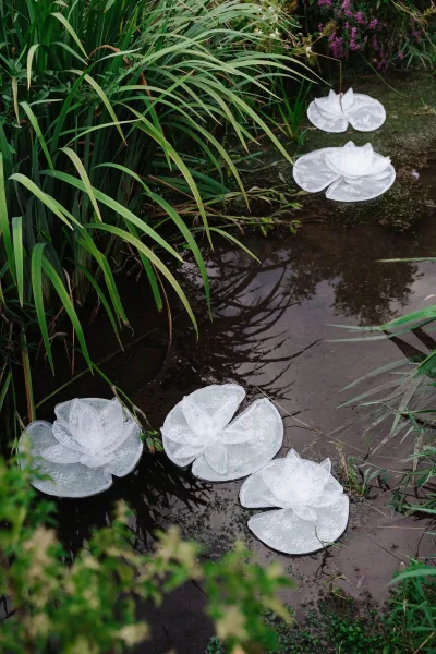 Floating floral decor with floating water lilies and lace florals drifting on a tranquil pond amid garden reeds, grasses, and shrubs.