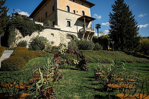 Outdoor wedding ceremony with garden wedding ceremony seating, wrought iron chairs and floral aisle arrangements on a stone terrace by a villa exterior
