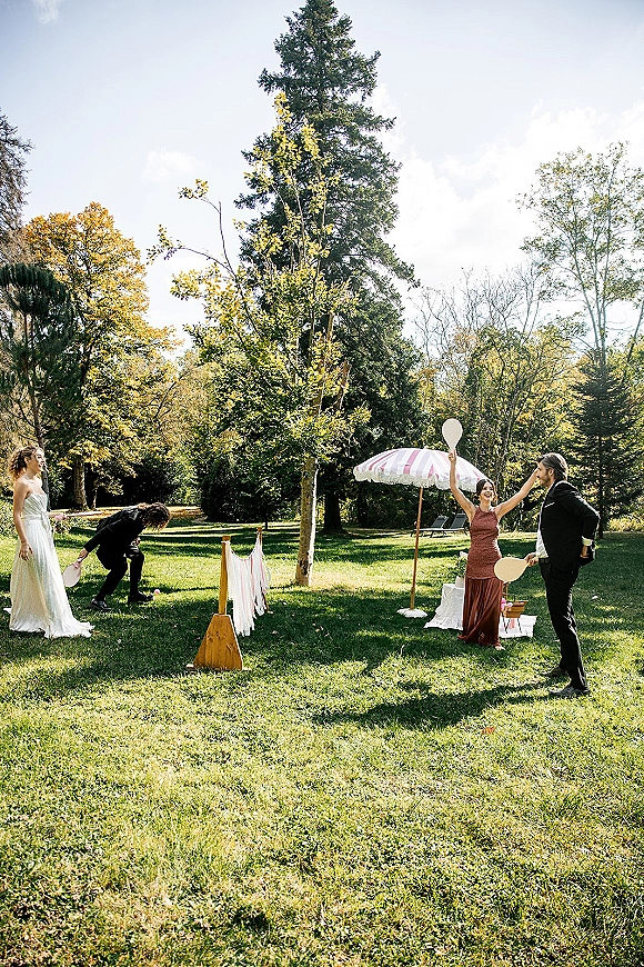 Wedding lawn games with wedding ping pong paddles on a netted table as bride and groom play on a sunny garden lawn under trees