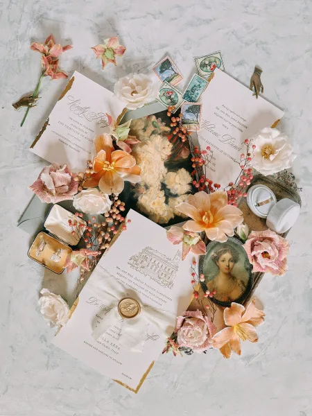 Invitation suite wedding invitation flat lay with deckle edge paper, wax seal, vintage stamps, and ring box arranged on light marble surface