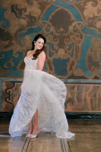Bridal portrait of a bride in a lace wedding dress with spaghetti straps and high slit, twirling by a painted mural wall indoors