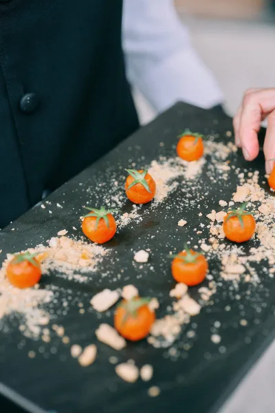 Wedding canapes on a black serving tray with cherry tomatoes and bite-size appetizers, held by a server in suit jacket in a neutral indoor space