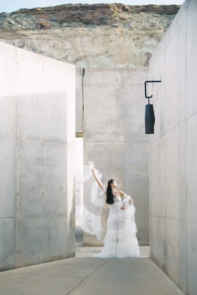 Bridal portrait of a bride in a strapless wedding dress with a flowing tulle veil, posed in an outdoor concrete corridor by a rocky cliff