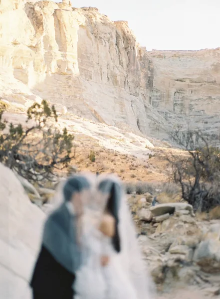 Wedding couple portrait of bride and groom outdoors on desert cliffs, bride’s veil blowing in wind above rocky landscape and sky