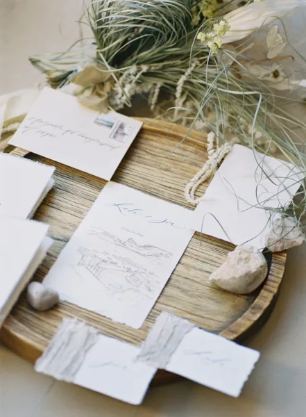 Invitation suite with deckled edge wedding invitations, calligraphy cards, ribbon and wax seal styled on a wood tray over linen tablecloth
