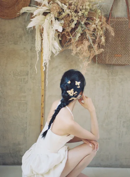 Bridal portrait of a side profile bride looking away, wearing a white mini wedding dress with butterfly hair pins by hanging dried florals on a plaster wall