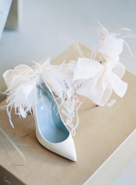 Bridal shoes, white wedding heels with feather shoe clips resting on a shoe box on a neutral floor in soft window light